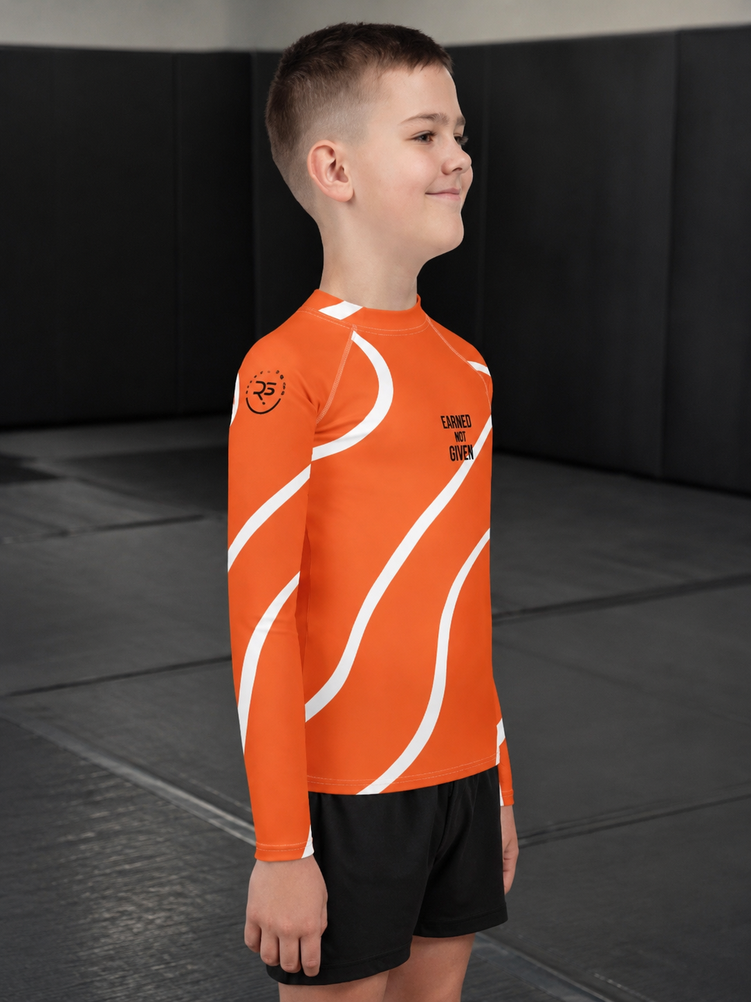 Child wearing an orange athletic shirt with white patterns in a gym setting