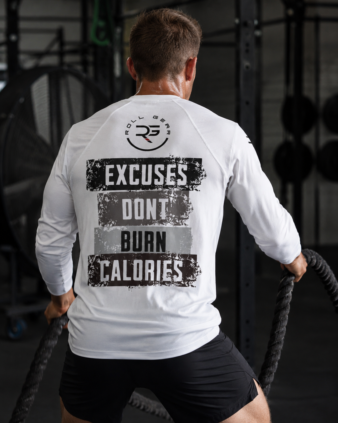 Person wearing a white long-sleeve shirt with motivational text in a gym setting