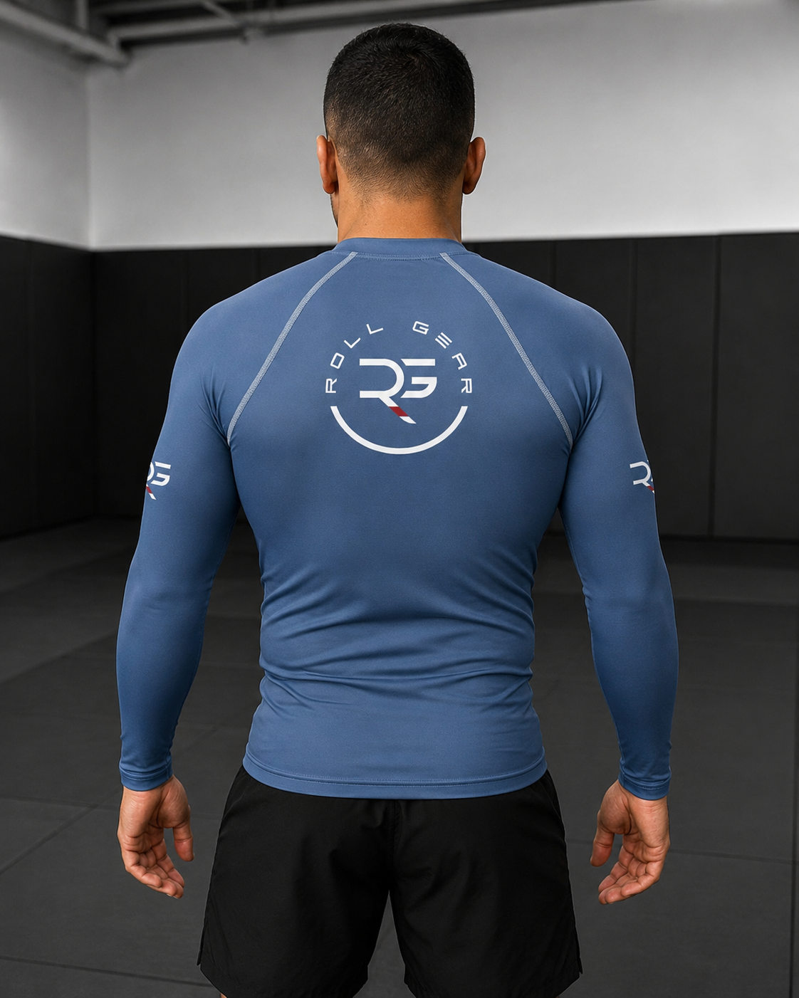 Person wearing a blue long-sleeve athletic shirt with a brand logo on the back, standing in a dark indoor setting.