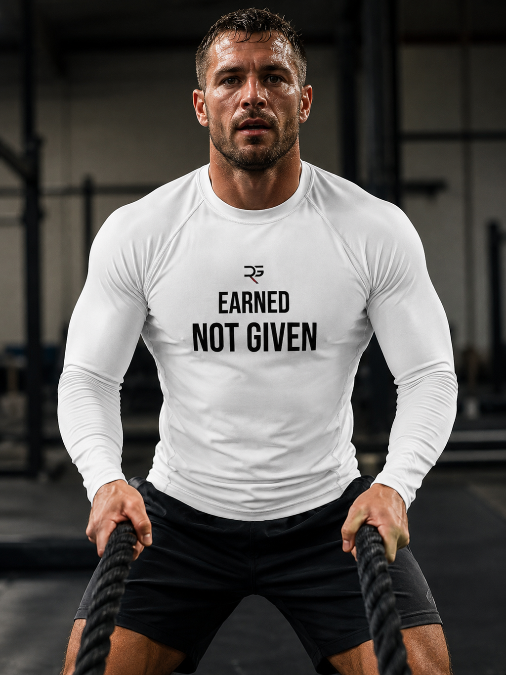 Man in a gym wearing a white long-sleeve shirt with 'Earned Not Given' text.