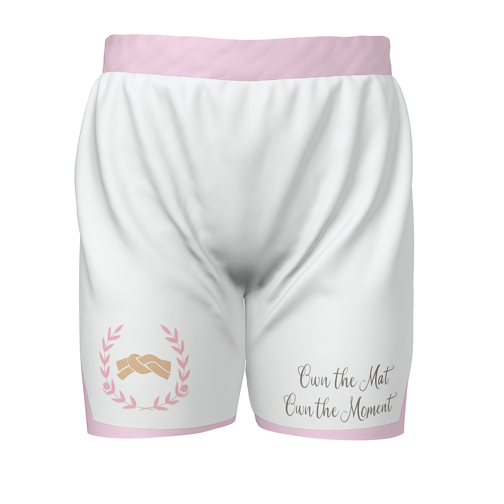 Front view of Roll Gear Kid’s 2-in-1 white athletic shorts with pink trim, featuring a laurel-wrapped grappling logo and “Own the Mat. Own the Moment” quote on the leg.