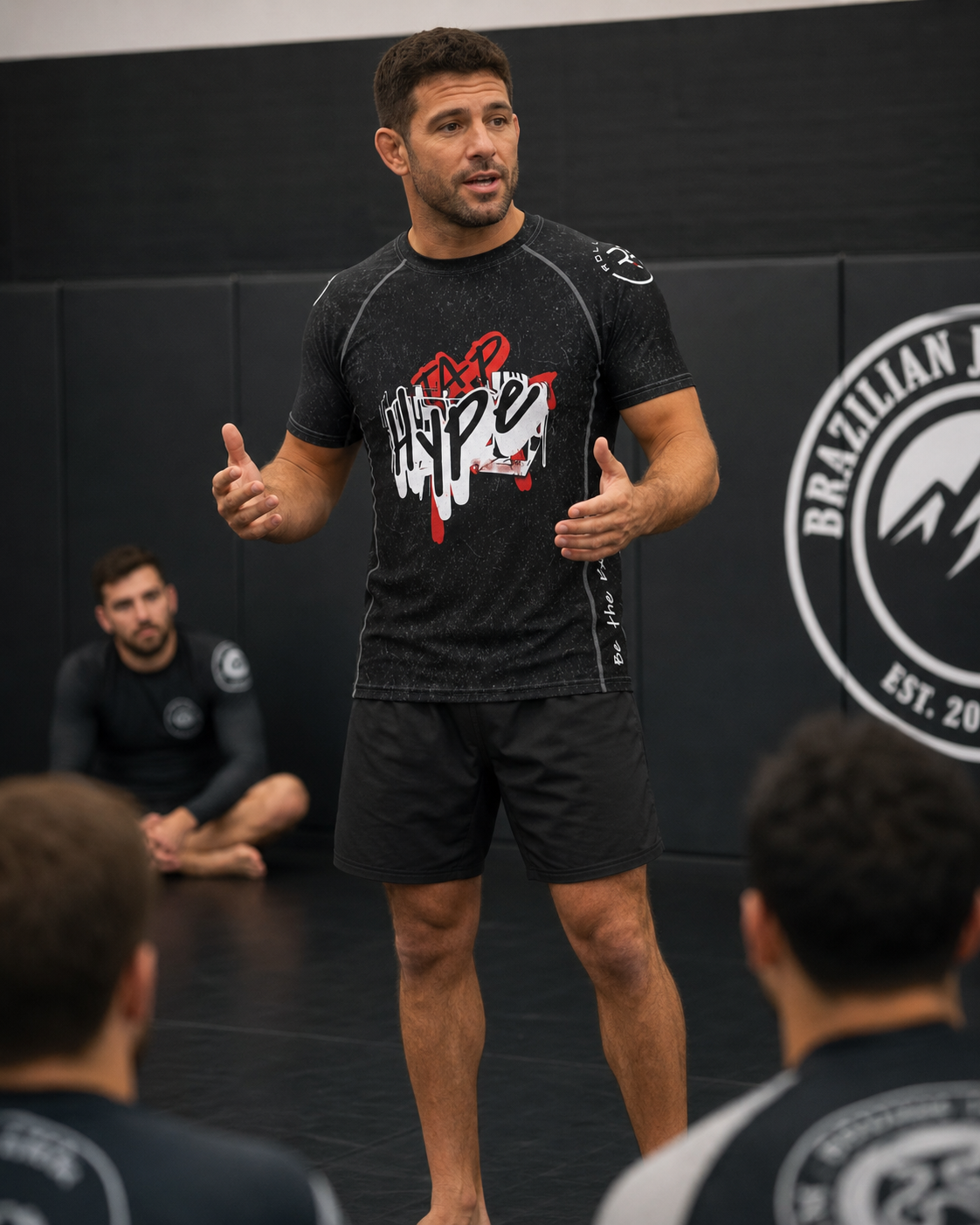 Man in athletic wear speaking to an audience in a Brazilian Jiu-Jitsu setting