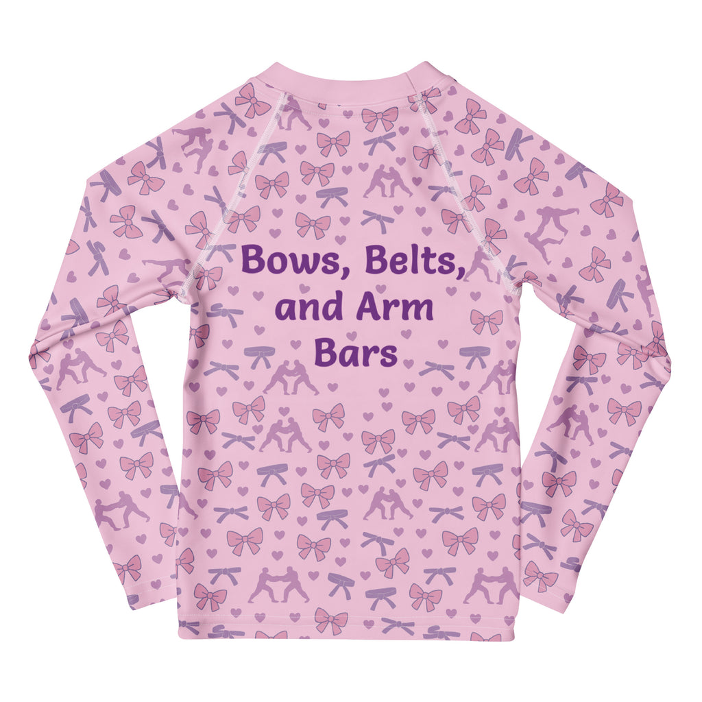 Pink long-sleeve shirt with bow and barbell pattern and text 'Bows, Belts, and Arm Bars' on a white background