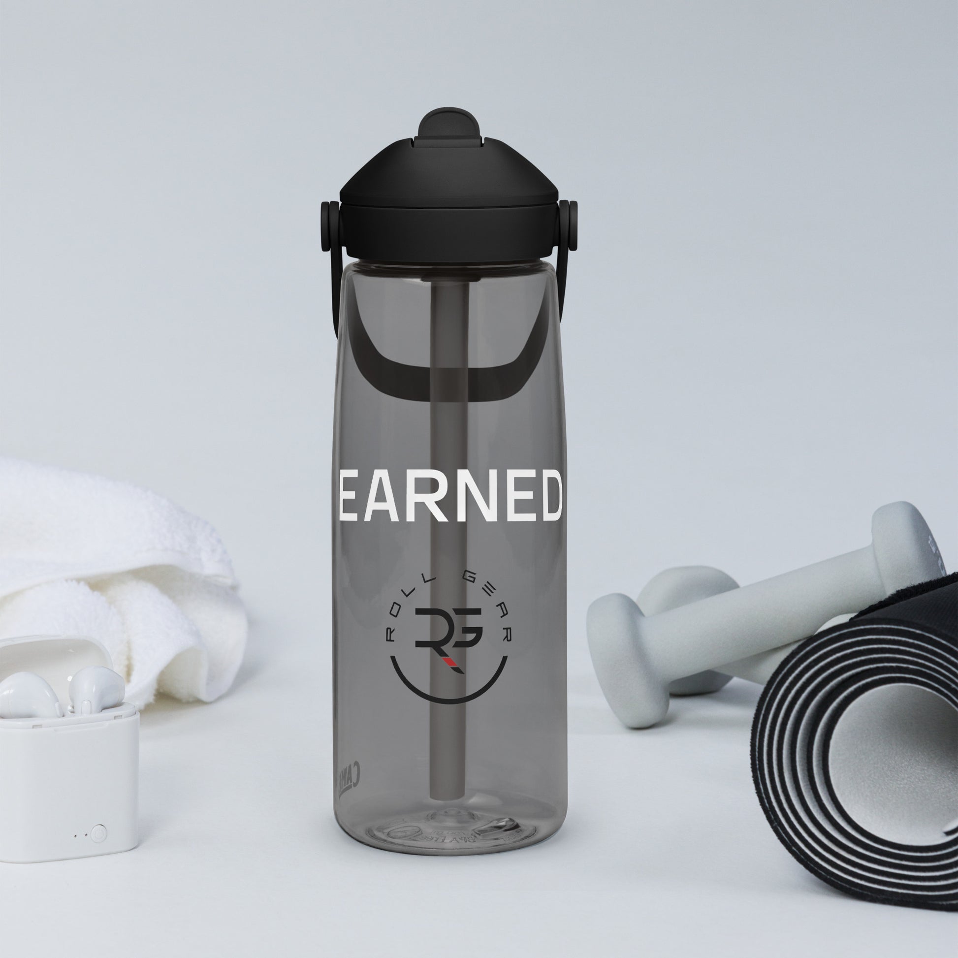 Lavender CamelBak water bottle with “EARNED.” print beside white sneakers and iPhone – minimalist gym scene showcasing Roll Gear’s active lifestyle branding