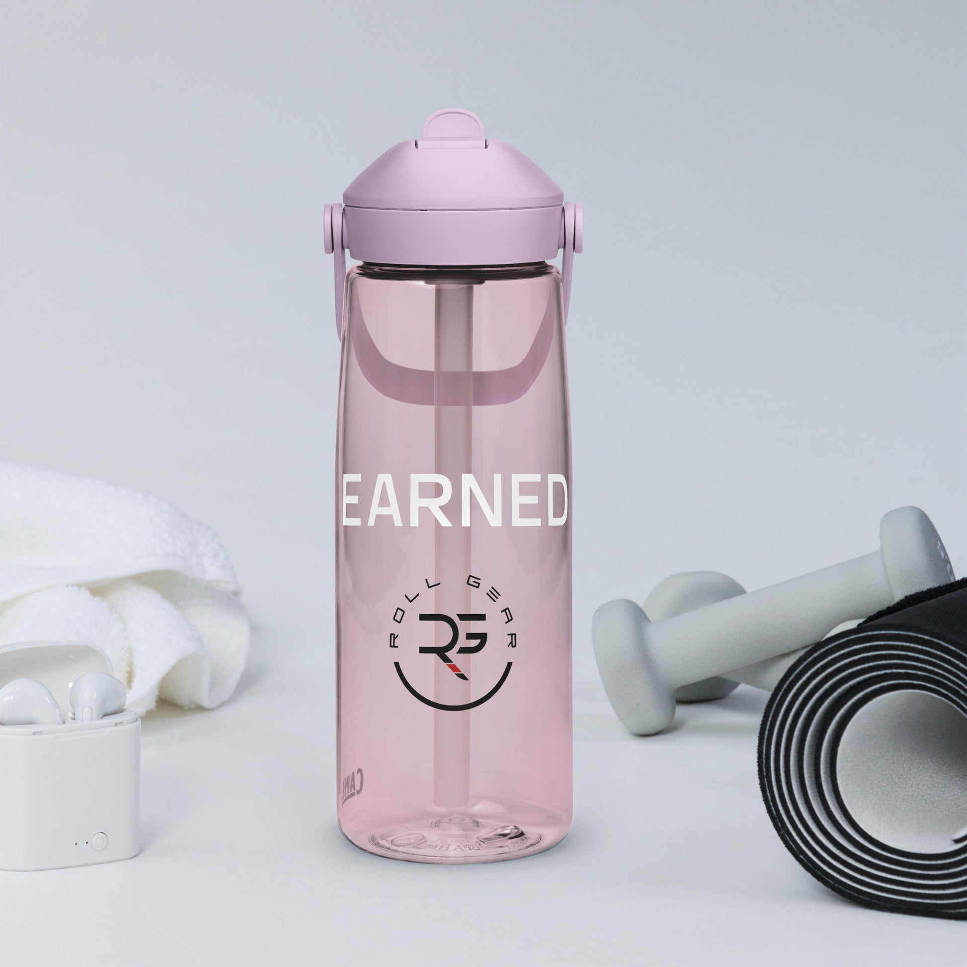 Lavender CamelBak water bottle with “EARNED.” print beside white sneakers and iPhone – minimalist gym scene showcasing Roll Gear’s active lifestyle branding