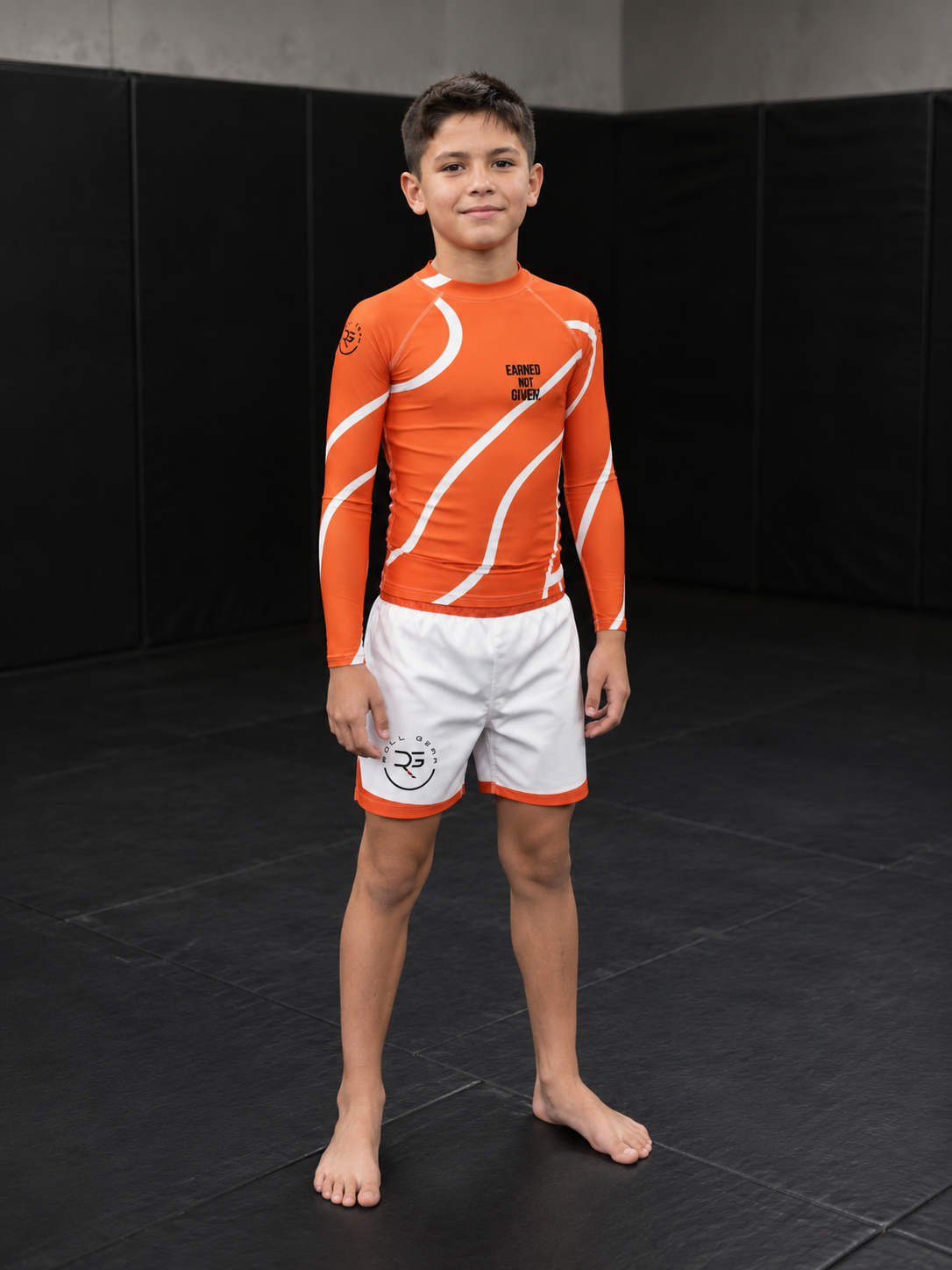 Child wearing an orange and white athletic outfit on a black mat