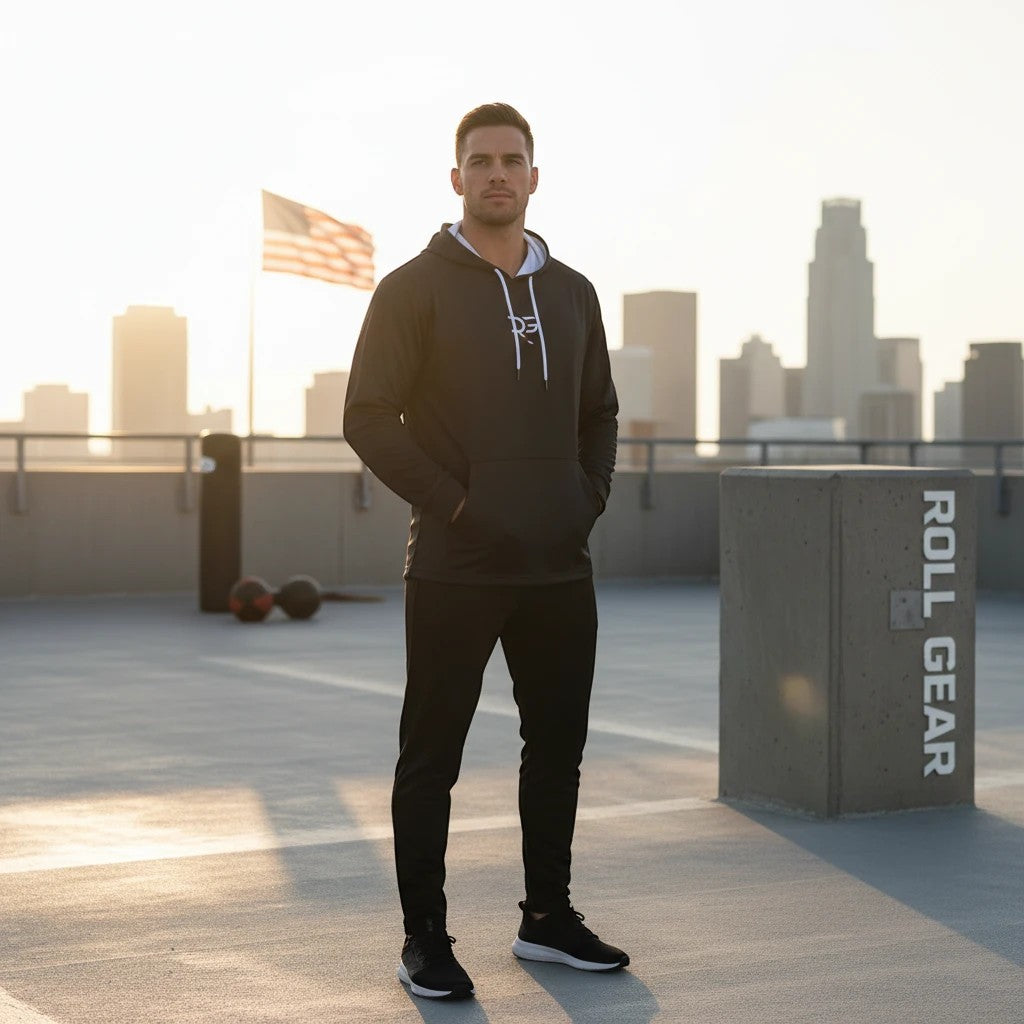 Roll Gear black performance long sleeve hoodie with white drawstring and chest logo, worn by a man standing outdoors.