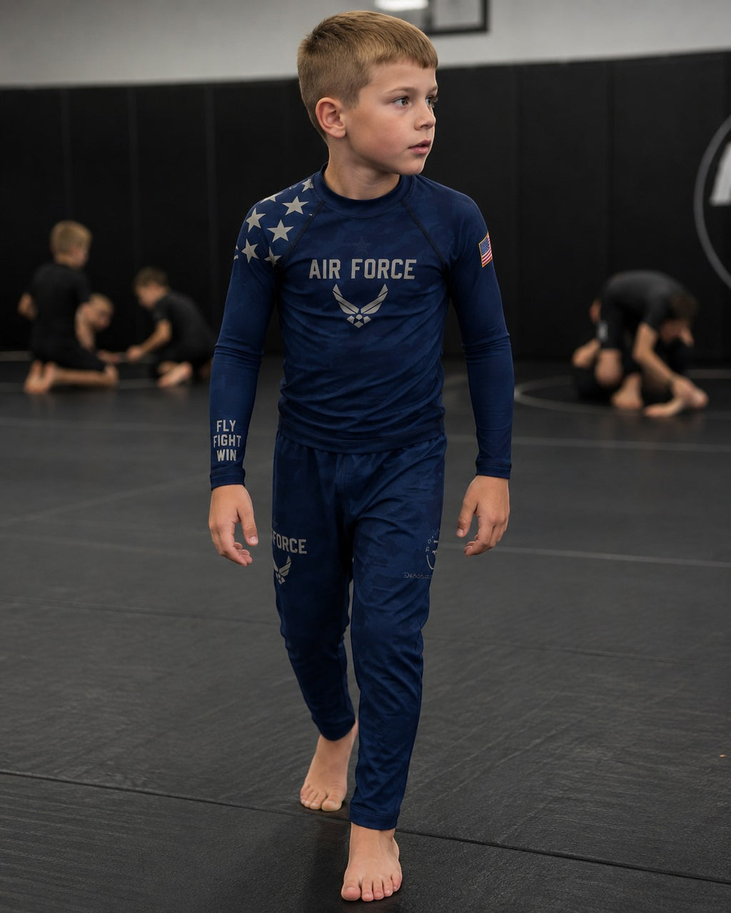 Roll Gear Kids Air Force blue long sleeve rash guard with silver graphics and matching pants, worn by a boy on a mat.