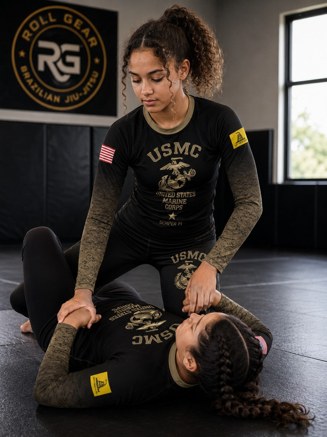 Roll Gear Kids Marines Gold military rash guard in black with faded gold sleeves and USMC emblem. Two girls training.
