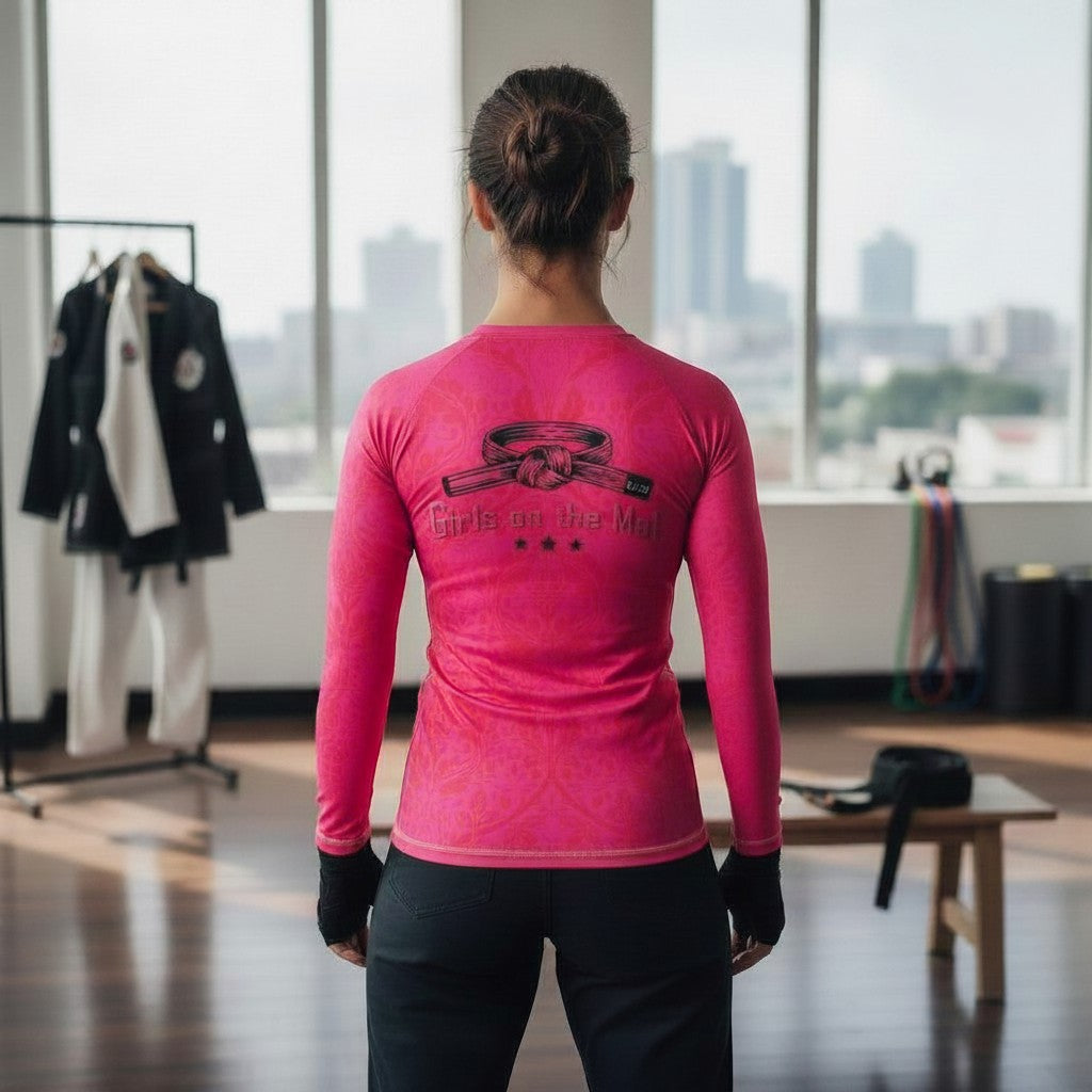 Roll Gear women's long sleeve rash guard in bright pink with a black belt graphic and "Girls on the Mat" text.